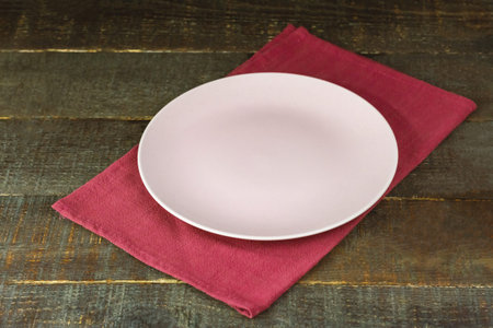 Empty pink plate on red tablecloth on rustic wooden table.