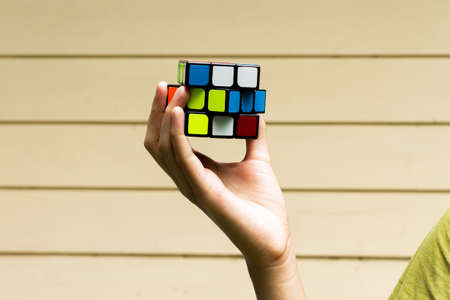 SAMUT-SAKHON, THAILAND - MAY 09, 2021 : Hands of young girl showing the Rubik's Cube puzzle on cream color background, Illustrative editorial.のeditorial素材