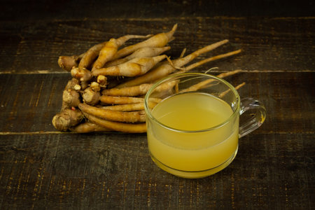 Finger root juice in transparent glass on rustic wooden background, dark tone. Finger root juice as...