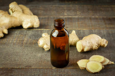 Ginger essential oil in bottle and fresh ginger on rustic wooden background. The scientific name is zingiber officinale. Herbs for health care concept.の写真素材