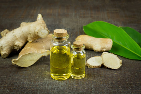 Ginger essential oil in bottle and fresh ginger on rustic wooden background. The scientific name is...