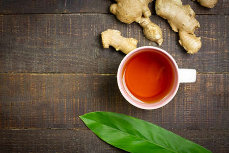 Ginger tea in ceramic cup and fresh ginger and sliced on wooden background, top view. The scientific name is zingiber officinale. Herbs for health care concept.の写真素材