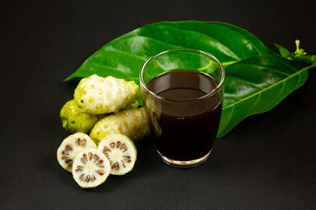 Noni juice in transparent and noni fruit with green leaf on black background.の写真素材