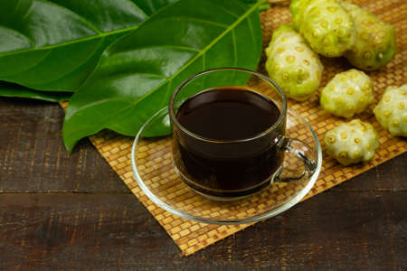 Noni juice in transparent glass and noni fruit with green leaf on wooden background.の写真素材