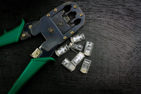 Modular plug crimper for RJ-45 with transparent connectors on black wooden background.