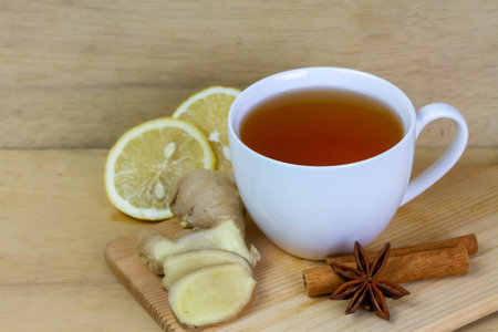 Cup of tea with ginger, lemon, cinnamon sticks and star anise on rustic wooden background.