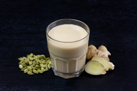 Glass cup of Masala chai tea with ginger and cardamom on black wooden background. Masala chai...