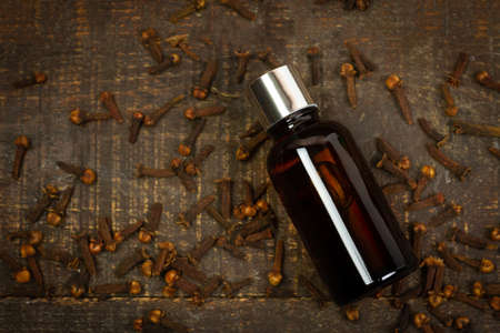 Essential oil of cloves in bottle and dry cloves on rustic wooden background, top view.の写真素材