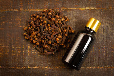 Essential oil of cloves in bottle and dry cloves on rustic wooden background, top view.の写真素材