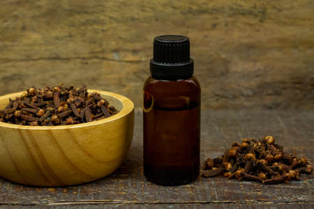 Essential oil of cloves in bottle and dry cloves on wooden bowl on rustic wooden background.の写真素材