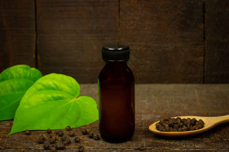 Black pepper essential oil in glass bottle with peppercorn on wooden spoon and green leaf on wooden background.の写真素材