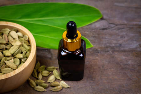 Cardamom essential oil in glass bottle with dry cardamom spice on wooden bowl and green leaf on rustic wooden background.の写真素材