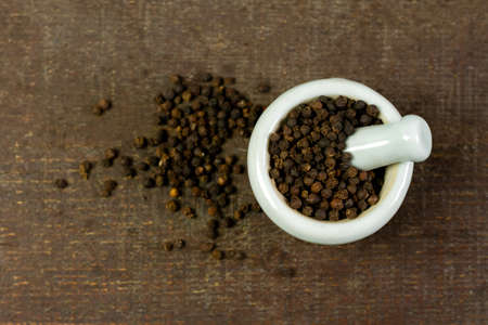 Black pepper in white mortar and pestle on wooden background top view. Black pepper is a spicy seasoning and herb for healthy.の写真素材