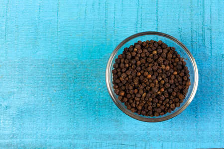 Black pepper in transparent glass bowl on blue wooden background. Black pepper is a spicy seasoning and herb for healthy.の写真素材