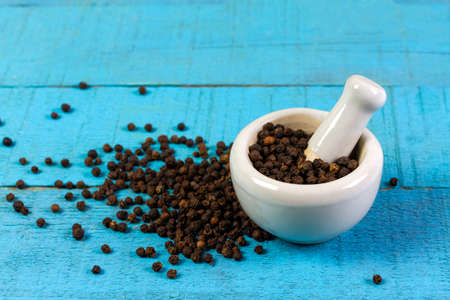 Black pepper in white mortar and pestle on blue wooden background. Black pepper is a spicy seasoning and herb for healthy.の写真素材