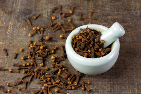 Cloves in white mortar with pestle on rustic wooden background. Herbal cloves have a fragrant and...