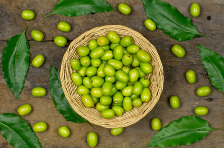Fresh Neem fruit on wicker basket with green leaf on wooden background. Neem fruit is an excellent moisturizing and contains various compounds that have insecticidal and medicinal properties.の写真素材