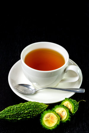 Bitter gourd or bitter melon tea in black cup on black wooden background. Scientific name is...