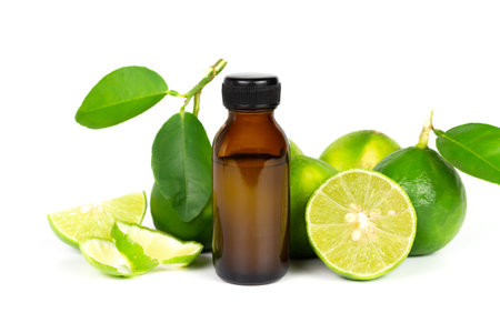 Lime essential oil in glass bottle and fresh lime fruits with green leaf isolated on white...