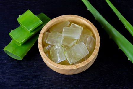 Aloe vera gel in wooden bowl with fresh aloe vera on black wooden background.の写真素材