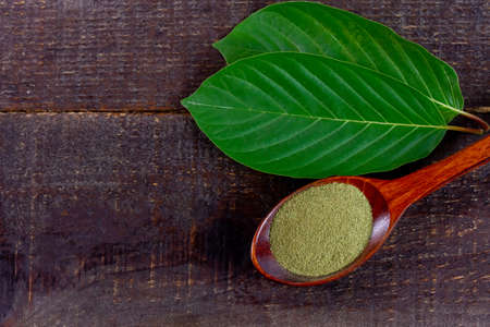Mitragyna Speciosa Korth or kratom powder on wooden spoon with green leaf on rustic wooden table, copy space, top view.の写真素材