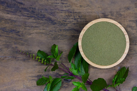 Holy basil powder on wooden bowl with branch on rustic wooden background, top view. Holy basil leaf...
