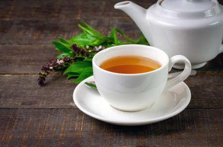 Basil tea in white cup ceramic with green leaf and white teapot on rustic wooden table. Basil is food and herb for healthy.の写真素材