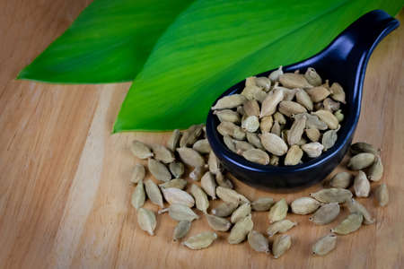 Green Cardamom on black bowl with green leaf and seed on wooden table. Cardamom is a fragrant herb used as an ingredient for cooking.の写真素材