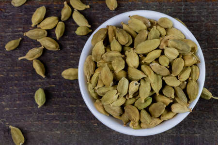 Green Cardamom on white bowl on rustic wooden table, top view. Cardamom is a fragrant herb used as an ingredient for cooking.の写真素材