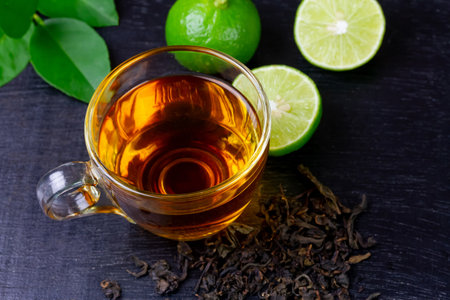 Hot tea in glass cup with fresh lime and leaf on black wooden background.の写真素材