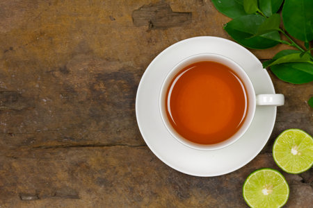Hot tea in white cup with fresh lime and green leaf on rustic wooden background, top view.の写真素材