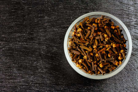 Cloves in white bowl on black wooden background, top view, copy space. Herbal cloves have a fragrant and spicy flavor.の写真素材