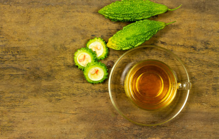 Bitter gourd or bitter melon tea in transparent cup and fresh bitter gourd on rustic wooden table, top view. Scientific name is Momordica charantia.の写真素材