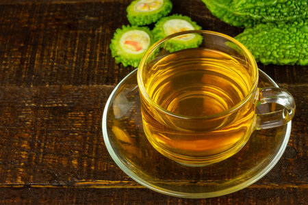 Bitter gourd or bitter melon tea in transparent cup and fresh bitter gourd on rustic wooden table. Scientific name is Momordica charantia.の写真素材