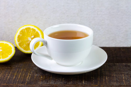 Cup of hot tea in white ceramic cup and fresh lemon on rustic wooden table and wihte background.の写真素材
