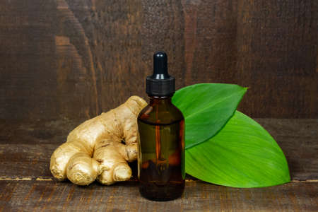 Ginger essential oil in bottle with fresh ginger and green leaf on rustic wooden background. The scientific name is zingiber officinale. Herbs for health care concept.の写真素材