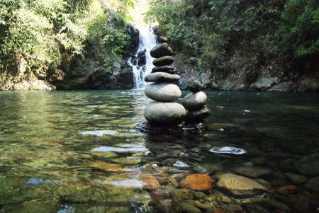 Stacked stones in the water of a mountain river, with a waterfall in the backgroundの写真素材