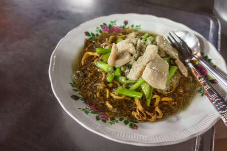 Crispy egg noodles with pork and Chinese kale in thick gravy. It on dishes on steel table background with copy space. For Asia food.の写真素材