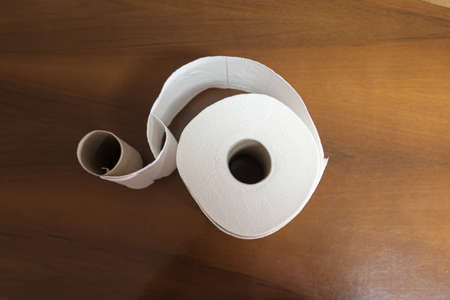 top view of an empty toilet paper roll intertwined with a new toilet paper roll on a dark wooden baseの写真素材