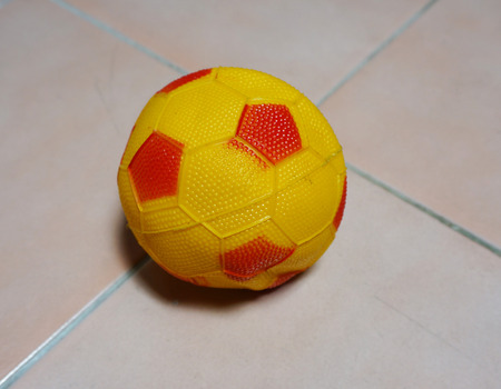 Soccer ball in yellow color with small red stripes. Placed on the floor at home                               の写真素材