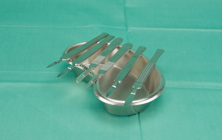 Many types of scalpel in kidney shape bowl on green fabric.の写真素材
