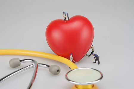 Miniature people are caring the heart and stethoscope put on table.の写真素材
