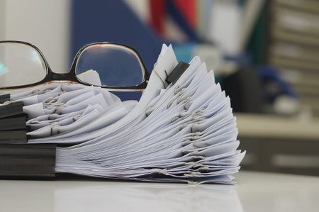 Glasses placed on finished document, stacks of paper files with clips on desk for report in the...