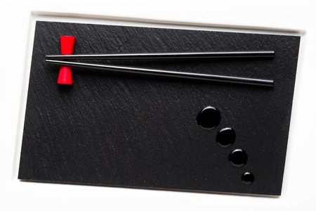 Chopsticks and soy sauce on white plate with black stone surfaceの写真素材