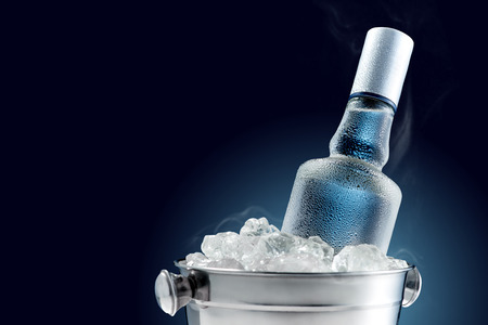 Bottle of cold vodka in bucket of ice on dark background Bottle of cold vodka in bucket of ice on dark background