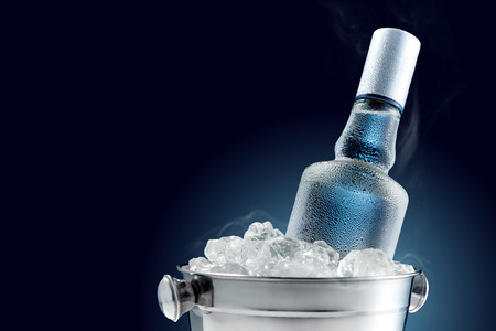 Bottle of cold vodka in bucket of ice on dark background