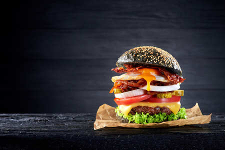 Black burger with egg and bacon on the wooden tableの写真素材