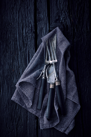 Old fashioned cutlery on kitchen towel on a black wooden backgroundの写真素材