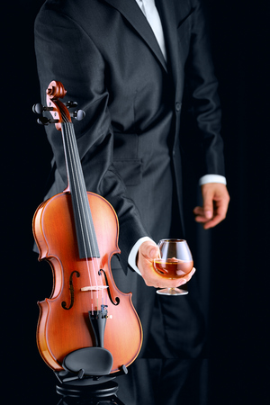 Violinist with glass of cognac and violin on dark backgroundの写真素材