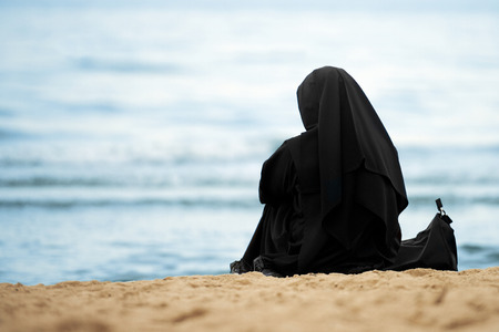 Muslim woman with black clothes sitting on the beachの写真素材